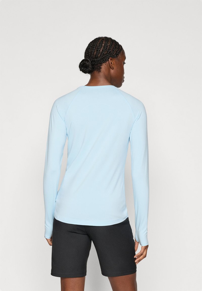 Jasnoniebieska bluzka z długim rękawem i rękawami raglanowymi, wykonana z gładkiego materiału; noszona z czarnymi szortami, podkreślająca wąski krój.