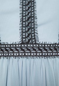 Tissu bleu clair avec une bordure en dentelle noire verticale et horizontale présentant des motifs géométriques et floraux, avec le tissu froncé sous la bordure.