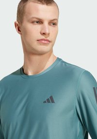 Türkisfarbenes Sportshirt aus strukturiertem Stoff, mit rundem Ausschnitt und schwarzen Logoakzenten auf der Brust und den Ärmeln.