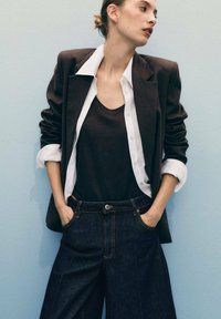 Brun blazer över en vit skjorta, ihop med en svart linne och vida denimjeans i mörk färg. Slätt tyg, skräddarsydd passform och strukturerad design.