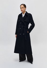 Czarny wełniany trencz z podwójnym rzędem guzików, paskiem w talii, szerokimi klapami oraz długą, prostą sylwetką z bocznymi kieszeniami.