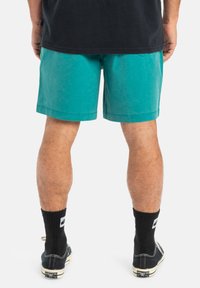 Turkosa bomullsshorts med rak passform, knälängd och enkel fåll. Bäres med svarta strumpor och avslappnade skor.