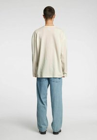 Lys beige langermet skjorte med avslappet passform, kombinert med lyseblå vide bukser og svarte sko, sett bakfra.