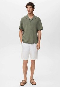 Short-sleeve green striped shirt with a collar, paired with white shorts and brown sandals, standing against a neutral background.