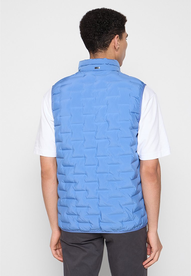 Hellblauer, wattierter Weste mit hohem Kragen, gerafftem Saum und ohne Ärmel, getragen über einem weißen Hemd. Schlichtes Design ohne sichtbare Beschläge.