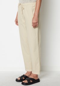 Beige Baumwollhosen mit Kordelzugbund, Seitentaschen und lockerem Schnitt. Kombiniert mit schwarzen Plattform-Sandalen mit Kreuzriemen.