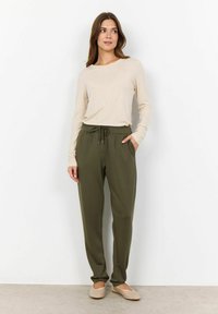 Beige long-sleeve top paired with olive green jogger pants featuring an elastic waistband and drawstring; slip-on beige shoes complete the outfit.