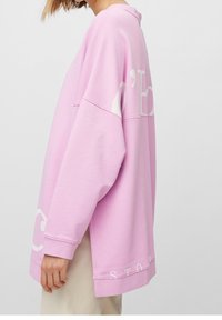 Sudadera rosa de gran tamaño, hecha de una mezcla de algodón, con mangas anchas y grandes letras blancas "C" y "STOK" en el dobladillo. Textura suave.