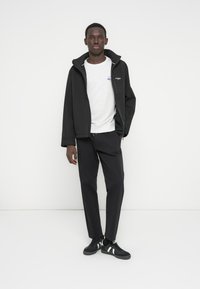 Black jacket with a zip, grey sweatshirt, and black pants. The outfit features a simple design and is complemented by black sneakers with white stripes.