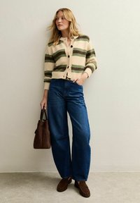 Cardigan beige con strisce verdi e marroni, abbottonato sul davanti, abbinato a jeans blu a vita alta, borsa a tracolla marrone e mocassini coordinati.