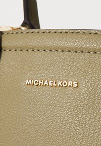 Olivi vihreä tekstuuroitu nahkainen käsilaukku, jossa on kultainen logo-akkentti, jossa lukee "MICHAEL KORS" edessä. Näkyvää ommeltu yksityiskohtia.