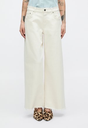Creamfarvede denimbukser med vide ben, flossede kanter, fem-lomme-design og sølvfarvet hardware. Sat sammen med leopardprint mules.
