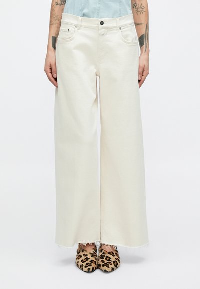 Pantalon en denim crème à jambes larges avec ourlet effiloché, design à cinq poches et garnitures en argent. Associé à des mules imprimé léopard.