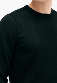 Schwarzer, gestrickter Rundhalsausschnitt-Pullover mit geripptem Halsausschnitt und Schulternähten, glatte Textur mit leichtem Glanz, Nahaufnahme.