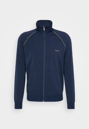 Navyblauwe ritsjack met hoge kraag, lange mouwen, twee frontzakken en contrasterende groene stiksels. Bevat een logo op de borst.