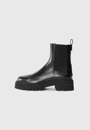 Botines de cuero negro con paneles elásticos en los lados, punta redonda y suela de goma gruesa que presenta un desgaste texturizado para mayor agarre.