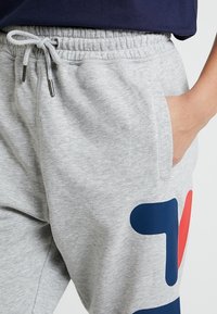Ljust grå sweatpants i mjukt bomullsmaterial; har resårmidja med dragsko och djärva grafiska inslag i marinblått och rött.