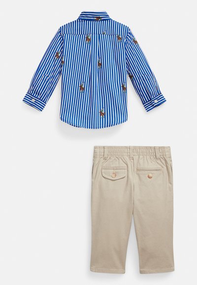 Μπλε και λευκό ριγέ μακρυμάνικο πουκάμισο με κέντημα παίκτη πόλο, σε συνδυασμό με μπεζ παντελόνι με κουμπωμένες πίσω τσέπες και ελαστική μέση.