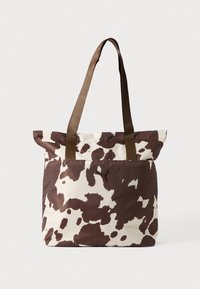 Sac fourre-tout en tissu doux avec un imprimé vache marron et crème, doté de deux anses marron pour les épaules et d'un détail logo.