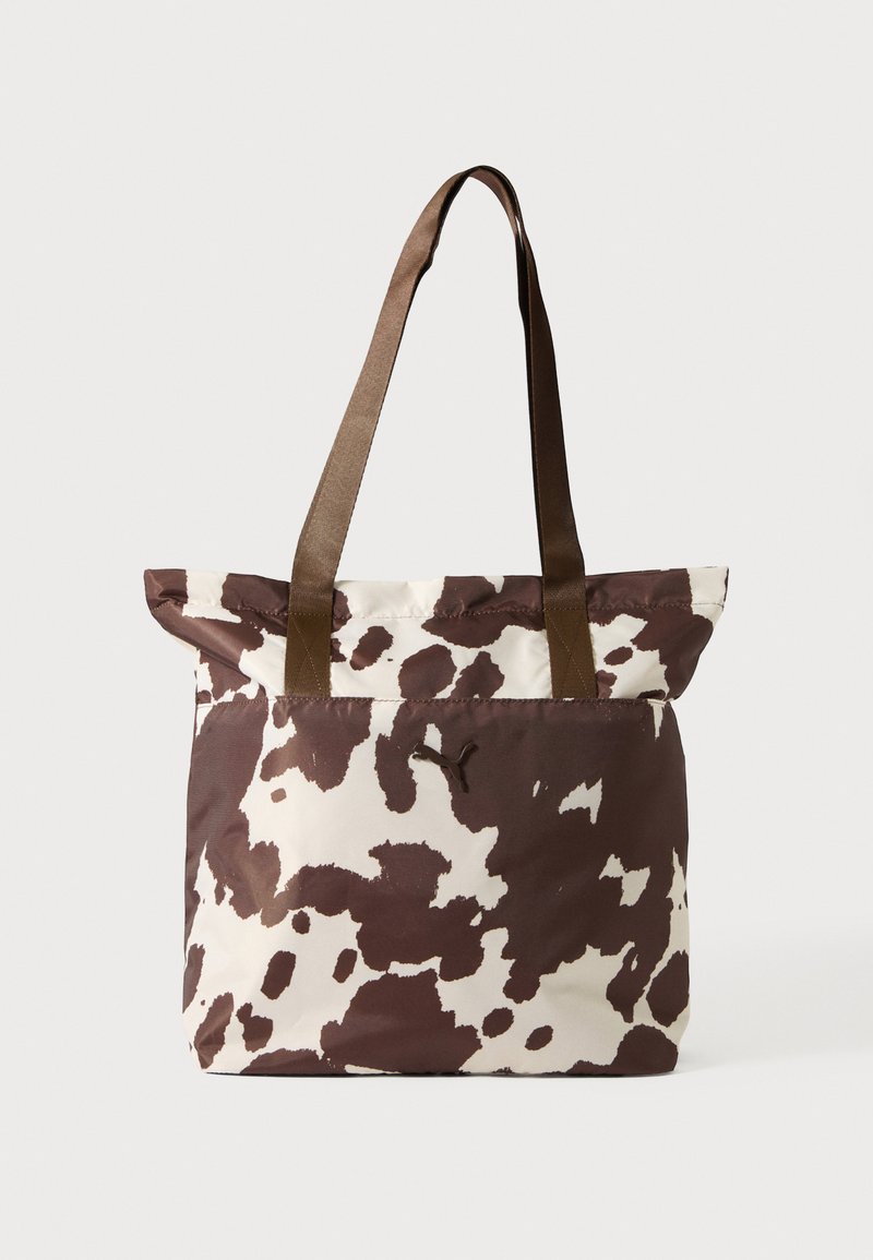 Sac fourre-tout en tissu doux avec un imprimé vache marron et crème, doté de deux anses marron pour les épaules et d'un détail logo.