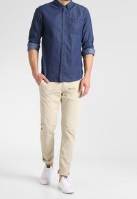 Knapp-up, mörkblå chambrayskjorta med uppvikta ärmar och ficka, tillsammans med ljusbeiga chinos och vita sneakers. Enkel, avslappnad outfit.