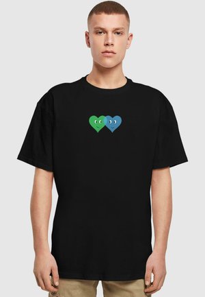 Sort t-shirt med et grafisk design af to hjerter, et grønt og et blåt, hver med smilende ansigt, placeret centralt på brystet.
