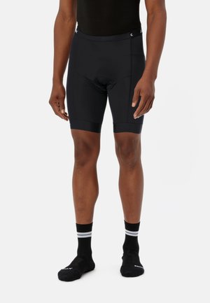 Zwarte fietsshorts voor heren met een gladde textuur, een aansluitend ontwerp en netaccenten aan de zijkanten; gecombineerd met zwarte sokken met witte strepen.