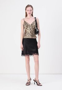 Gul leopardmönstrad cami, svart kjol med spetsdetaljer, svarta högklackade sandaler och en liten svart handväska. Släta texturer, åtsittande design.