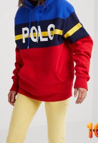 Sudadera roja y azul con gran texto en blanco "POLO", franjas amarillas y marinas. Cuenta con un bolsillo frontal, capucha con cordón y puños acanalados.