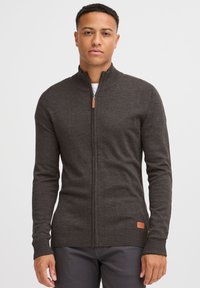 Dunkelgraue Reißverschlussstrickjacke aus strukturiertem Wolle. Mit gerippten Bündchen und Saum, sowie einem Lederakzent nahe dem Boden.