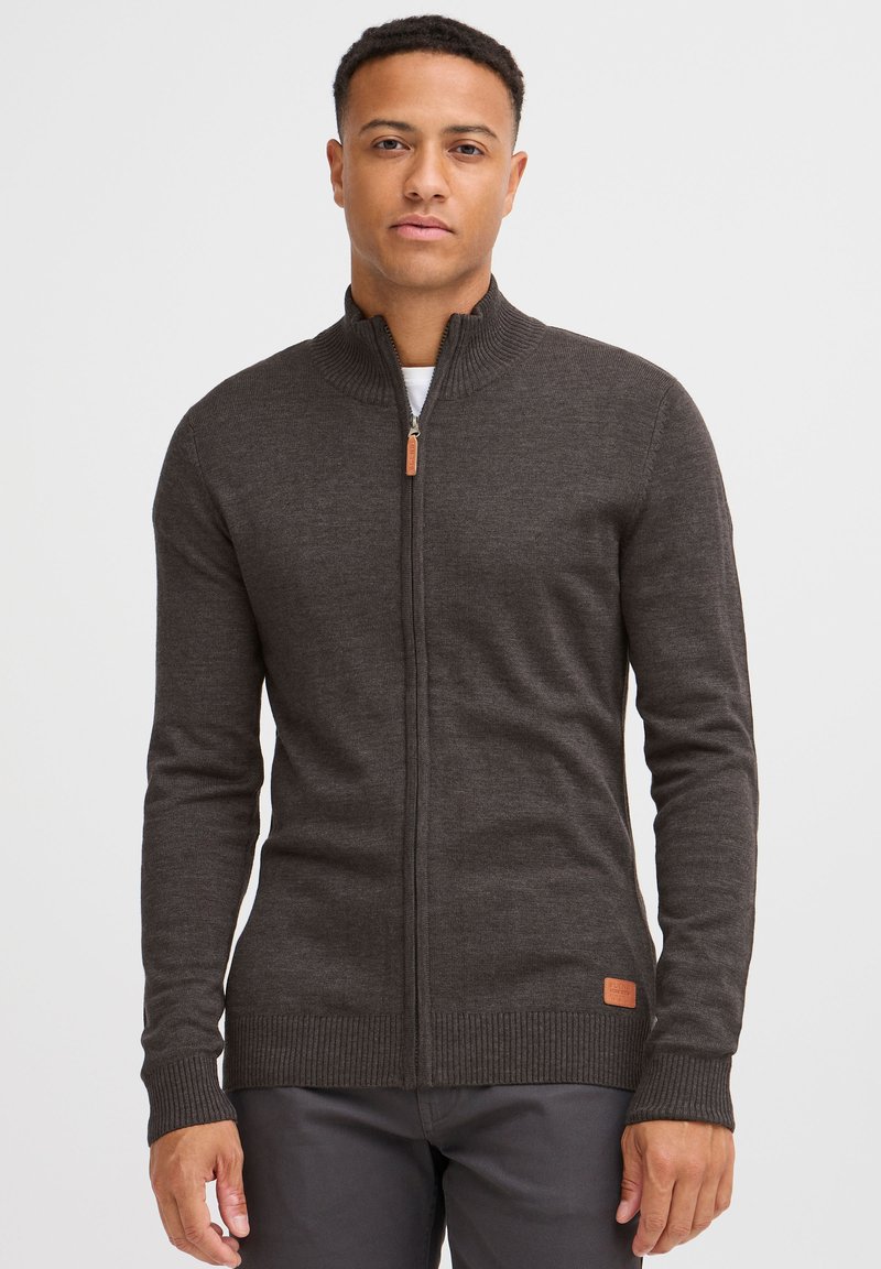 Dunkelgraue Reißverschlussstrickjacke aus strukturiertem Wolle. Mit gerippten Bündchen und Saum, sowie einem Lederakzent nahe dem Boden.