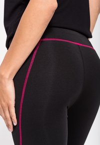 Leggings neri con un design aderente, caratterizzati da una cucitura rosa a contrasto lungo il lato e da una texture di tessuto liscia e elastica.