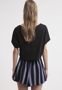 Top negro cortado combinado con una falda acampanada a rayas en tonos de azul, negro y blanco, que presenta líneas verticales y un tejido texturizado.