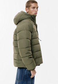 Giubbotto imbottito verde oliva con cappuccio, dotato di sezioni trapuntate, zip frontale e polsini elasticizzati, abbinato a una parte superiore scura in contrasto.