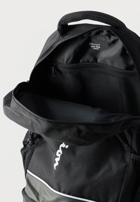 Μαύρο σακίδιο με κεντρικό χώρο με φερμουάρ και διχτυωτή θήκη. Διαθέτει λευκό λογότυπο και κομψό σχέδιο με λεία υφή.