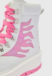 Witte hoge laarzen met roze accenten; glanzend materiaal, patroon op de zijkant, roze veters, zilveren oogjes en dikke roze rubberen zool.