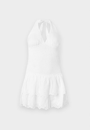 Witte halterjurk met een gesmockte bovenkant en een gelaagde rok. Heeft een gegolfde rand en gaatjesdetail aan de onderkant. Zachte katoenen textuur.