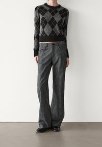 Pull en tricot noir et gris à motif argyle associé à un pantalon large gris à rayures, avec poches avant et fermeture boutonnée. Texture lisse, coupe décontractée.