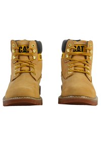 Bottes de travail en cuir tan avec une marque jaune et noire, œillets dorés et lacets jaunes. Dotées d'un col rembourré gris et d'une semelle brune texturée.