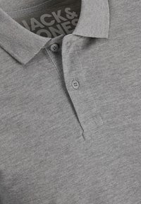 Polo gris avec une texture douce, présentant un col, deux boutons gris et le logo "Jack & Jones" visible à l'intérieur de l'encolure.