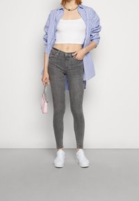 Jeans ajustados grises, top corto blanco y una camisa a rayas azul. Sosteniendo un pequeño bolso rosa, combinado con zapatillas blancas.
