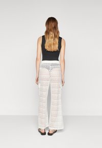 Pantalons larges en dentelle blanche avec un motif, portés sur un haut noir. Les pantalons ont une coupe ample et présentent un aspect texturé et léger.
