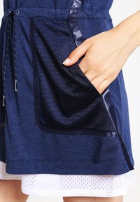 Navy blue sporty dress featuring a textured mesh pocket, smooth navy accents, and a drawstring waist. The hem includes white mesh detailing.