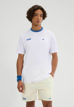 Camiseta blanca de manga corta con cuello redondo azul y logo; combinada con pantalones cortos amarillos claros y una pulsera azul. Textura de tela suave.