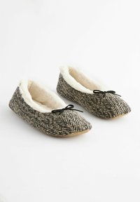 Black and white herringbone-patterned slippers with a soft cream lining, rounded toe, and black ribbon bow detail. Flat, flexible soles.