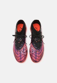 Zwarte sportschoenen met een gestructureerde, paars en roze gradient bovenkant, voorzien van zwarte veters, oranje binnenzolen en een witte logoaccent.