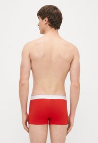 Sarkanas bokseršorti ar baltu elastīgu jostu, kurā ir plāna zila un sarkana svītra. Ērts piegriezums, gluda auduma tekstūra, minimālistisks dizains.