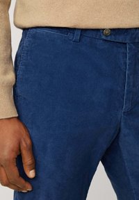 Pantaloni in corduroy di un blu profondo, caratterizzati da un design a coste testurizzato. Inclusa una chiusura con bottone e una silhouette aderente.