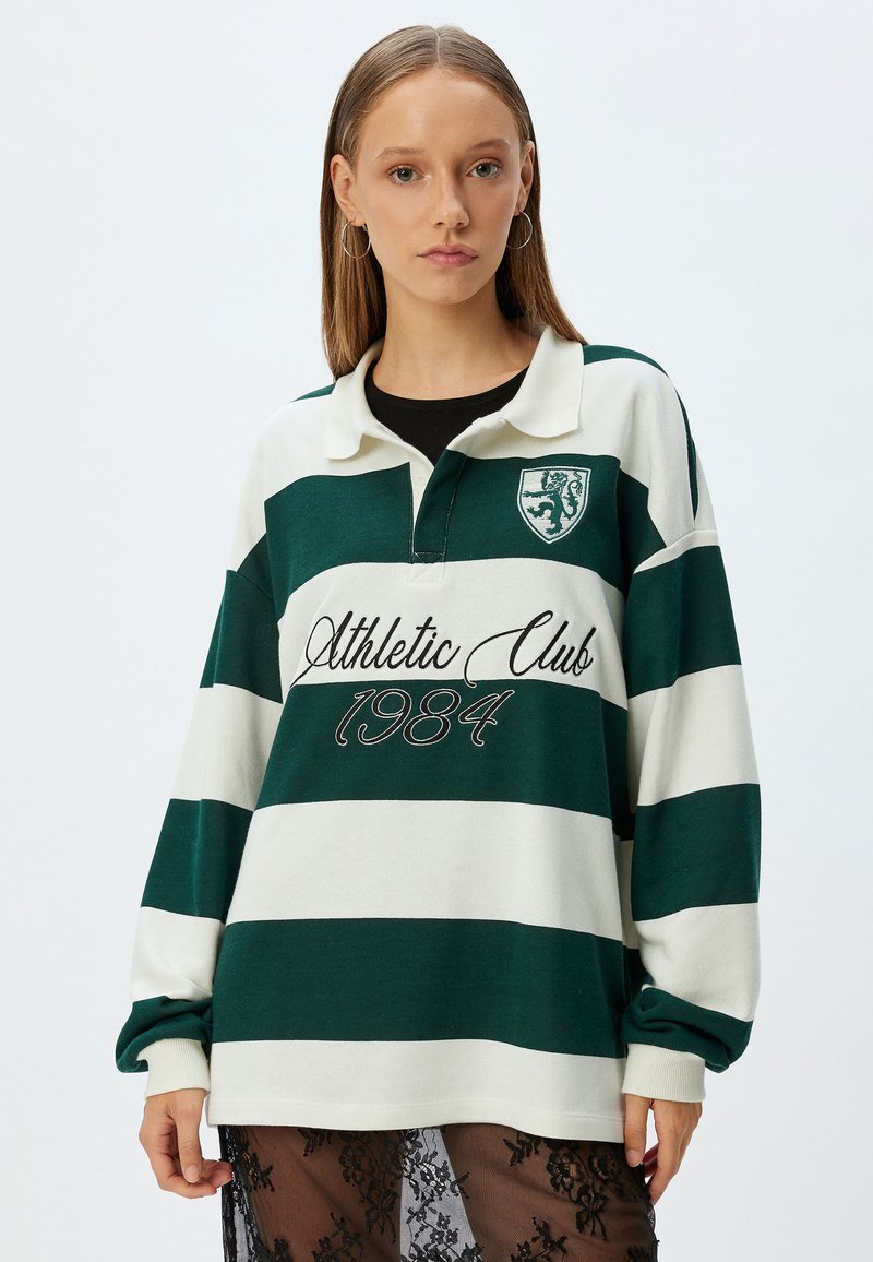 Vihreä ja valkoinen raidallinen rugby-tyylinen paita, jossa on kaulus, ja jossa on brodeerattu vaakuna sekä "Athletic Club 1984" edessä. Pitkät hihat.