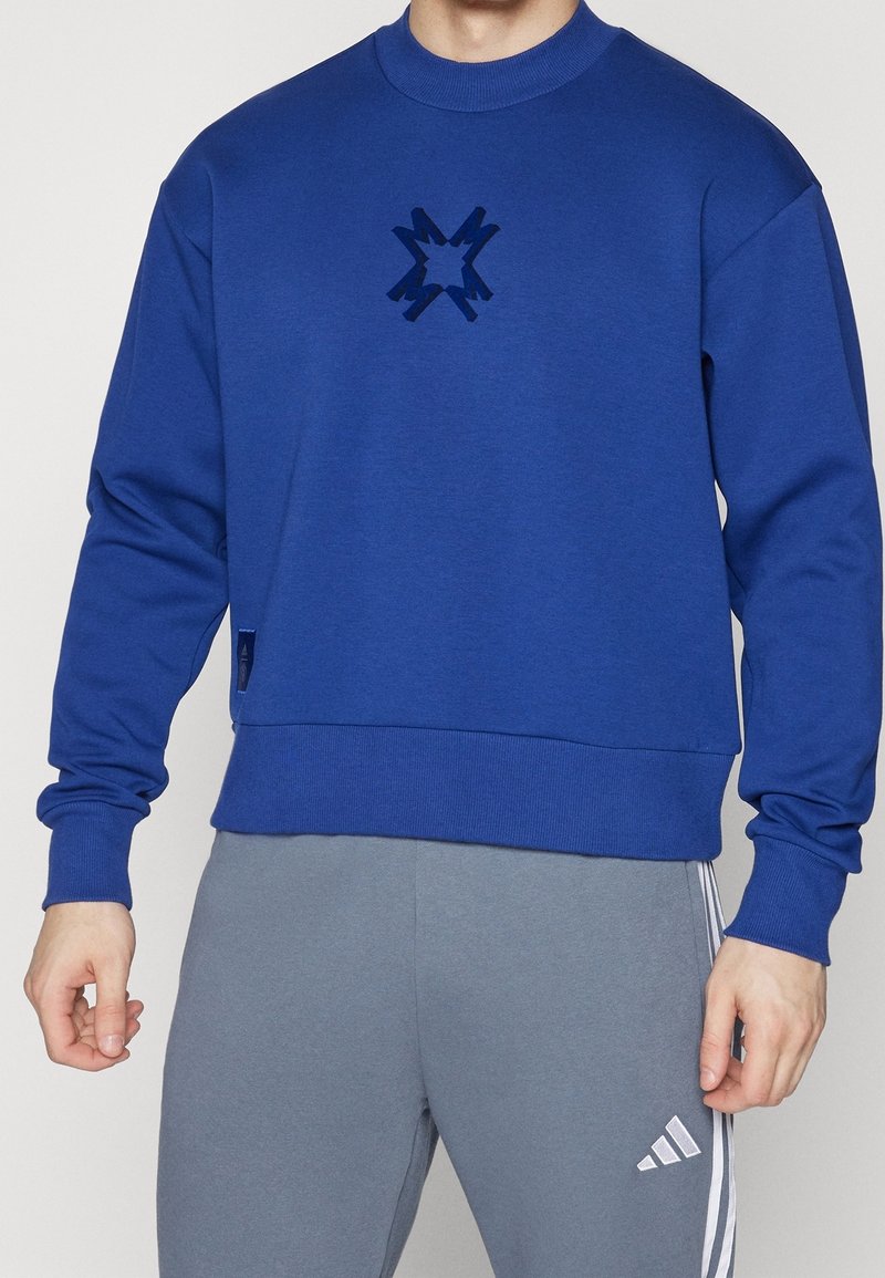 Felpa blu con scollo rotondo e polsini a coste. Presenta un design di stelle scure e lucide al centro e una vita aderente.